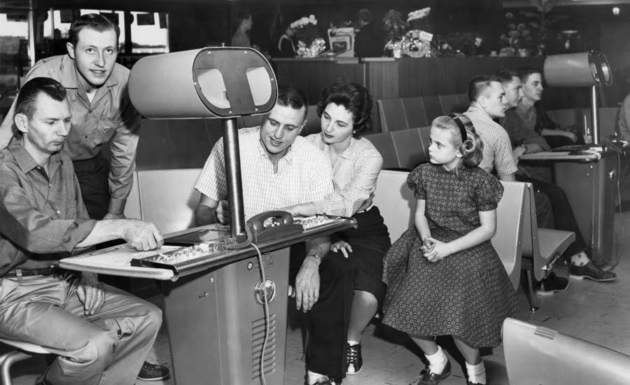 Vintage bowlers gathered around a manual overhead scoring console